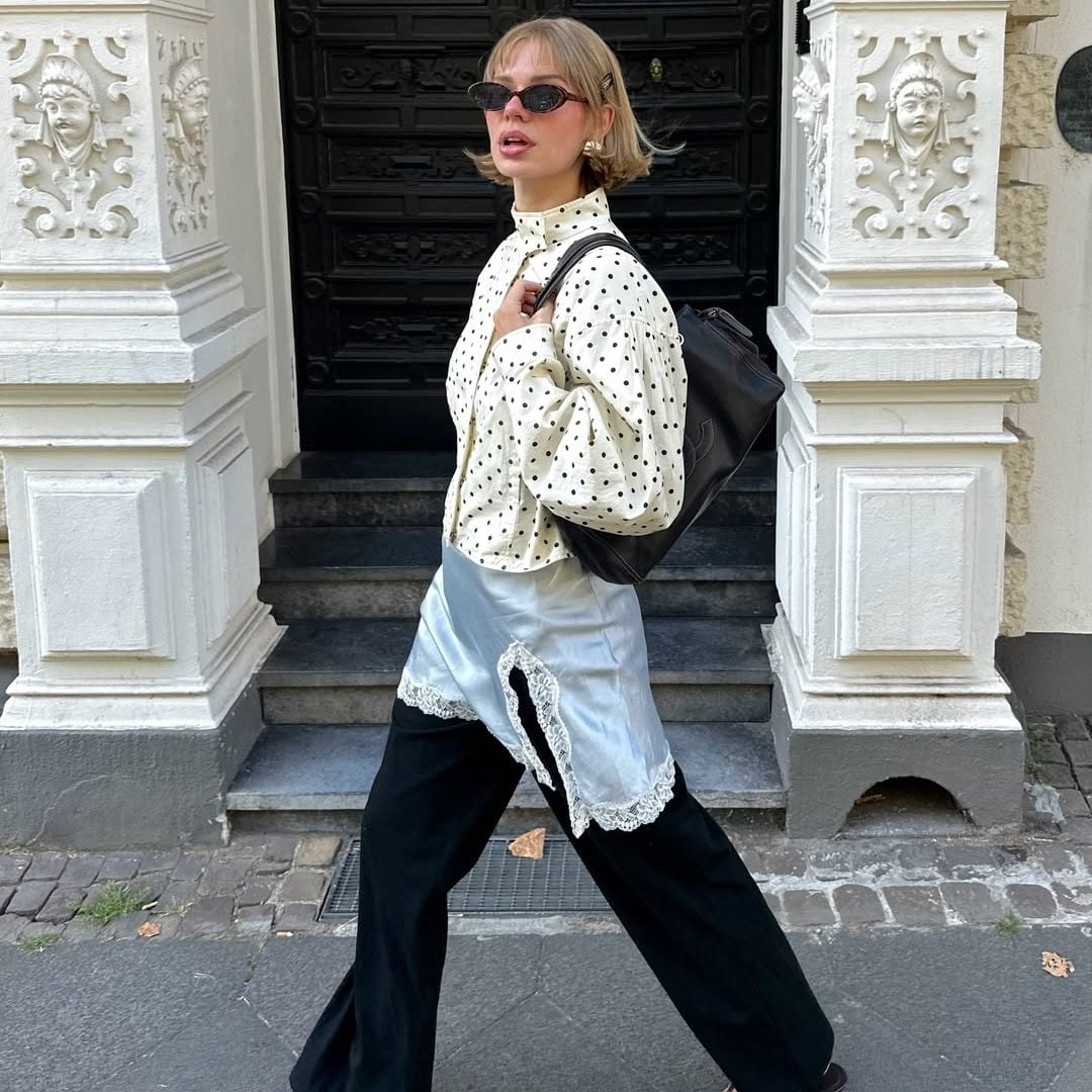 Γυναίκα με street style look που συνδυάζει cropped πουά τζάκετ, γαλάζιο σατέν lingerie τοπ με δαντέλα, μαύρο υφασμάτινο παντελόνι και μαύρα πέδιλα με kitten τακούνι.
