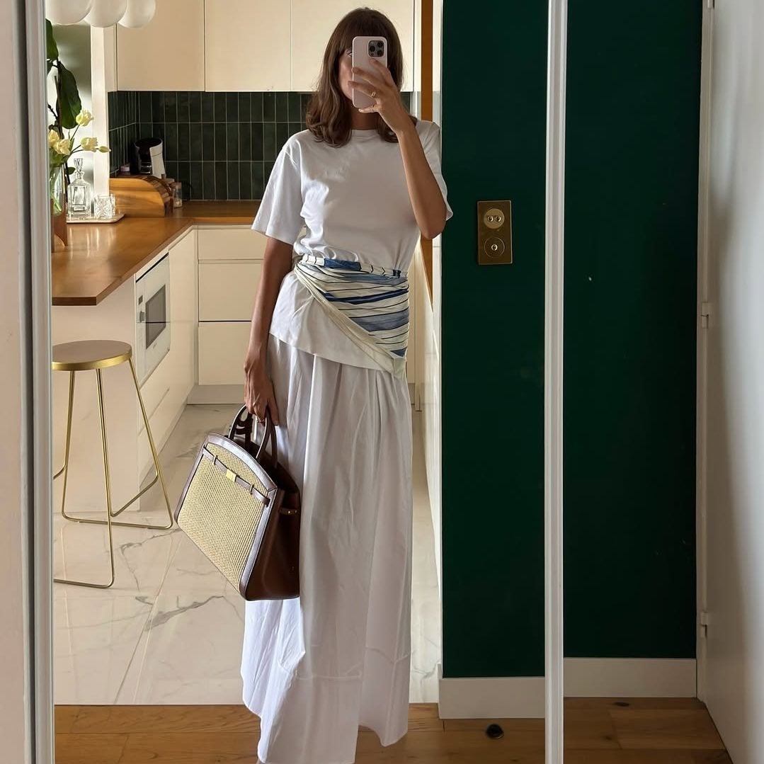Μια luxury υφαντή tote τσάντα με καφέ δερμάτινα λουριά ολοκληρώνει ιδανικά ένα καλοκαιρινό λευκό σύνολο, προσθέτοντας premium υφή.
