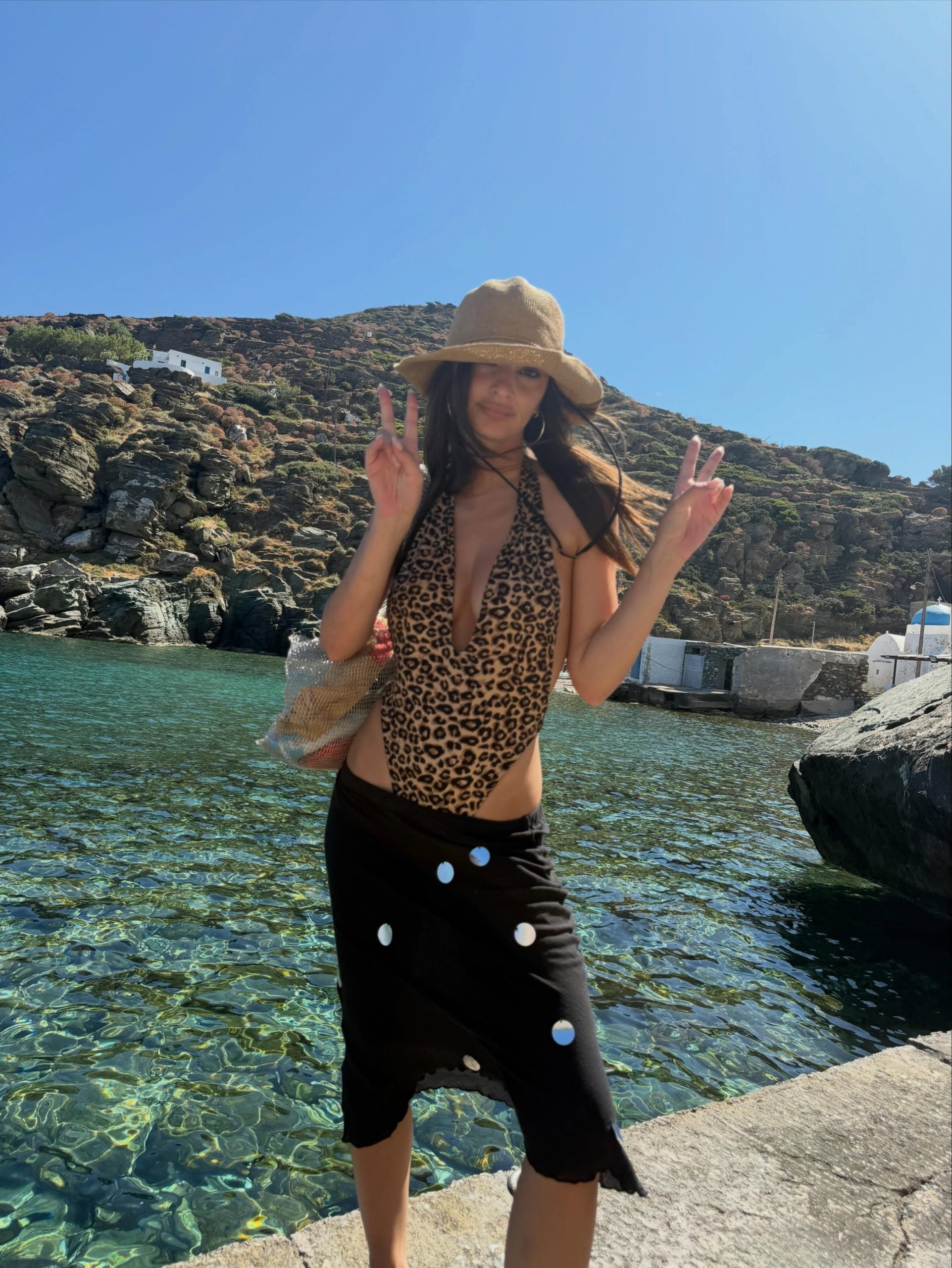 Η Emily Ratajkowski παραδίδει μαθήματα αιχμηρού beachwear στην Ελλάδα, συνδυάζοντας λεοπάρ ολόσωμο μαγιό με μαύρη ανάλαφρη φούστα.