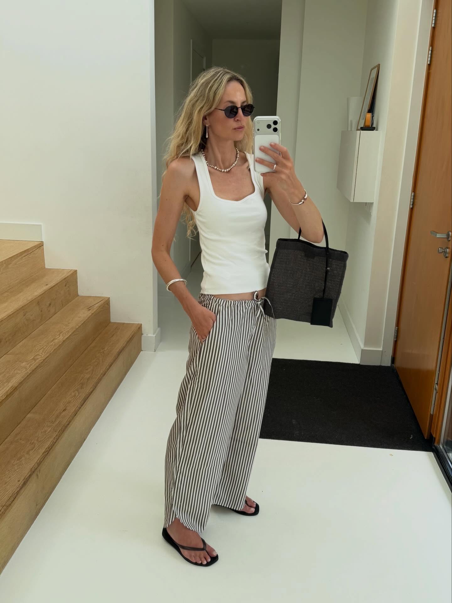 Ένα look που βασίζεται στα essentials της γκαρνταρόμπας. Λευκό tank top, αέρινο ριγέ παντελόνι και μίνιμαλ αξεσουάρ. Τα μαύρα σανδάλια, η tote τσάντα και τα διακριτικά κοσμήματα ολοκληρώνουν ένα κομψό σύνολο.
