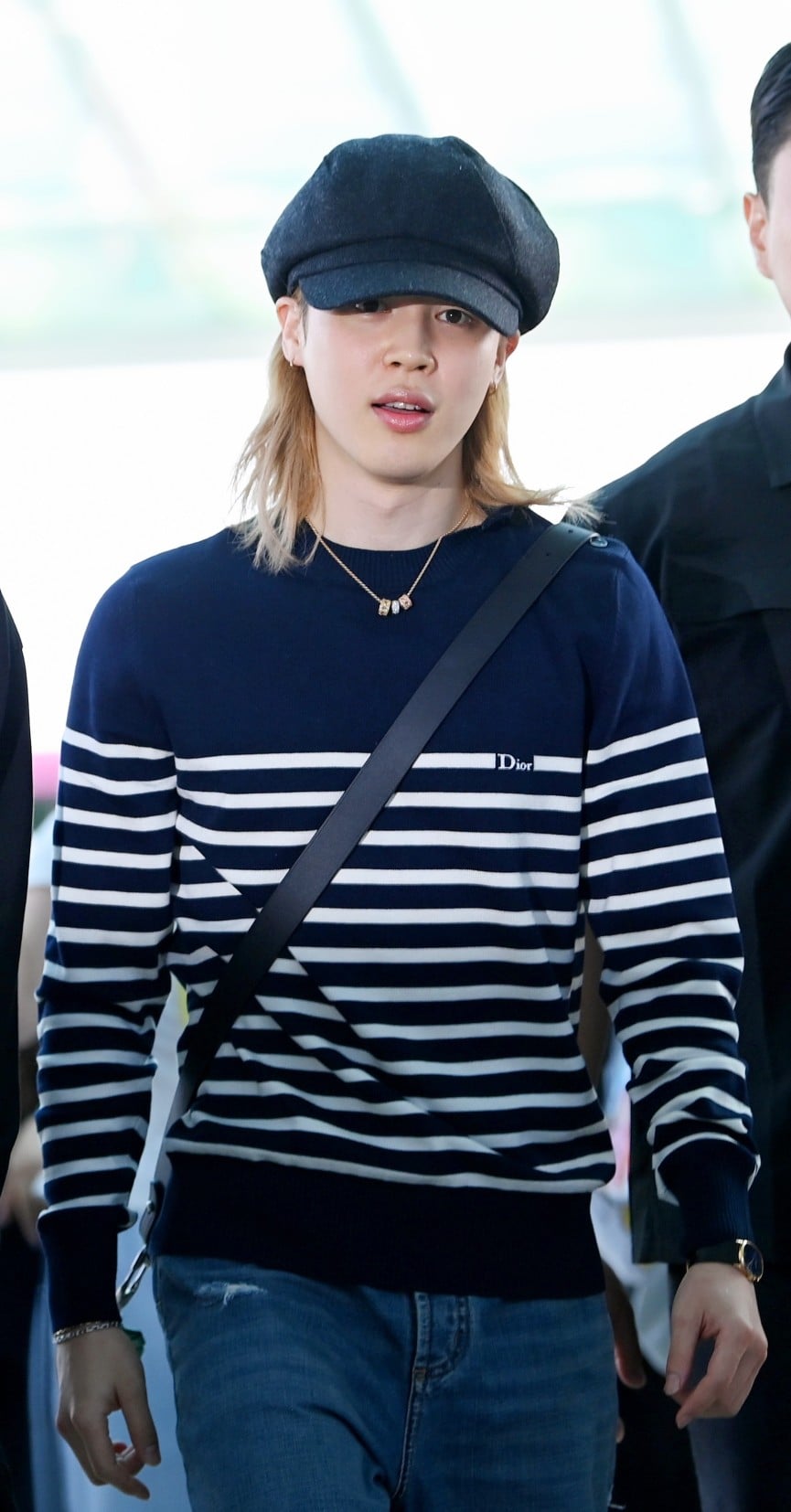 Ο Jimin με Dior σε ένα effortless airport look, συνδυάζοντας ριγέ μπλε και λευκό μάλλινο sweater με μπλε denim jeans. Ολοκλήρωσε την εμφάνισή του με μαύρη δερμάτινη Dior Archie zipped bag και ένα εντυπωσιακό My Dior κολιέ από κίτρινο, ροζ και λευκό χρυσό, διακοσμημένο με διαμάντια.